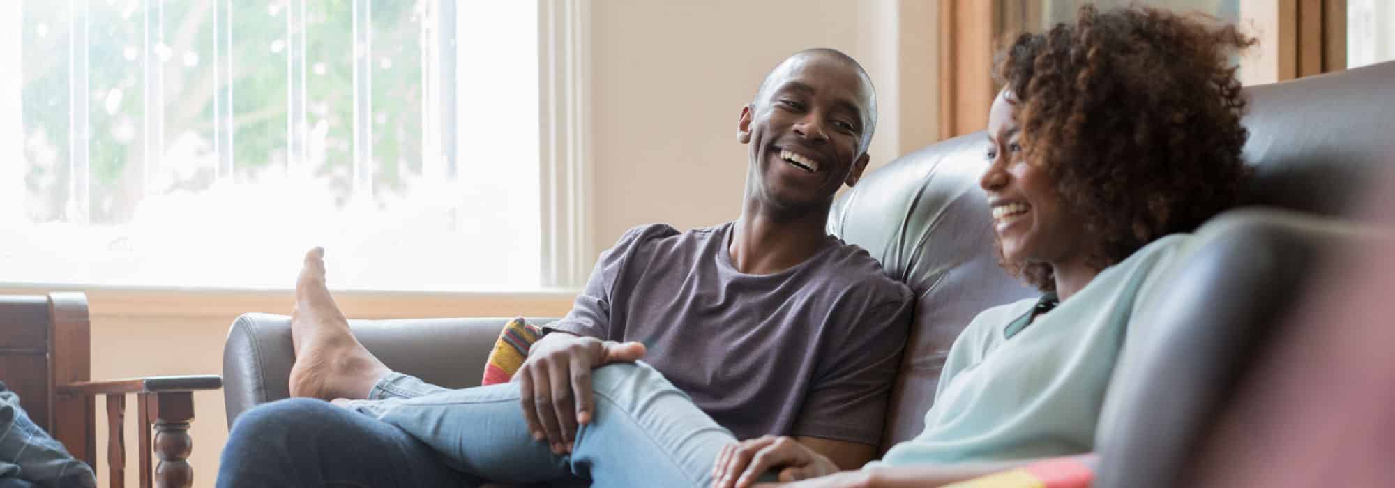 A couple lounging on the couch. They are laughing.