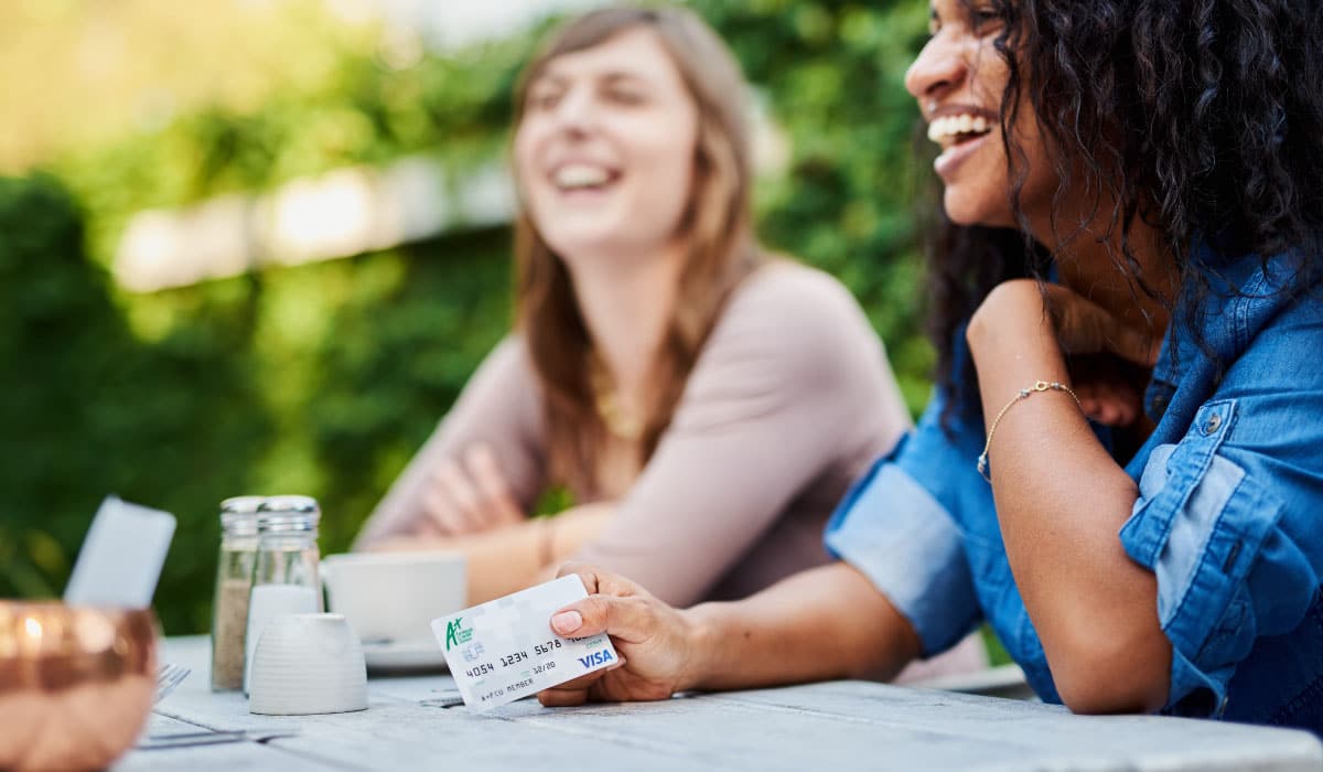 Two friends sitting at a table and laughing. One of them is holding an A+ Debt Card.