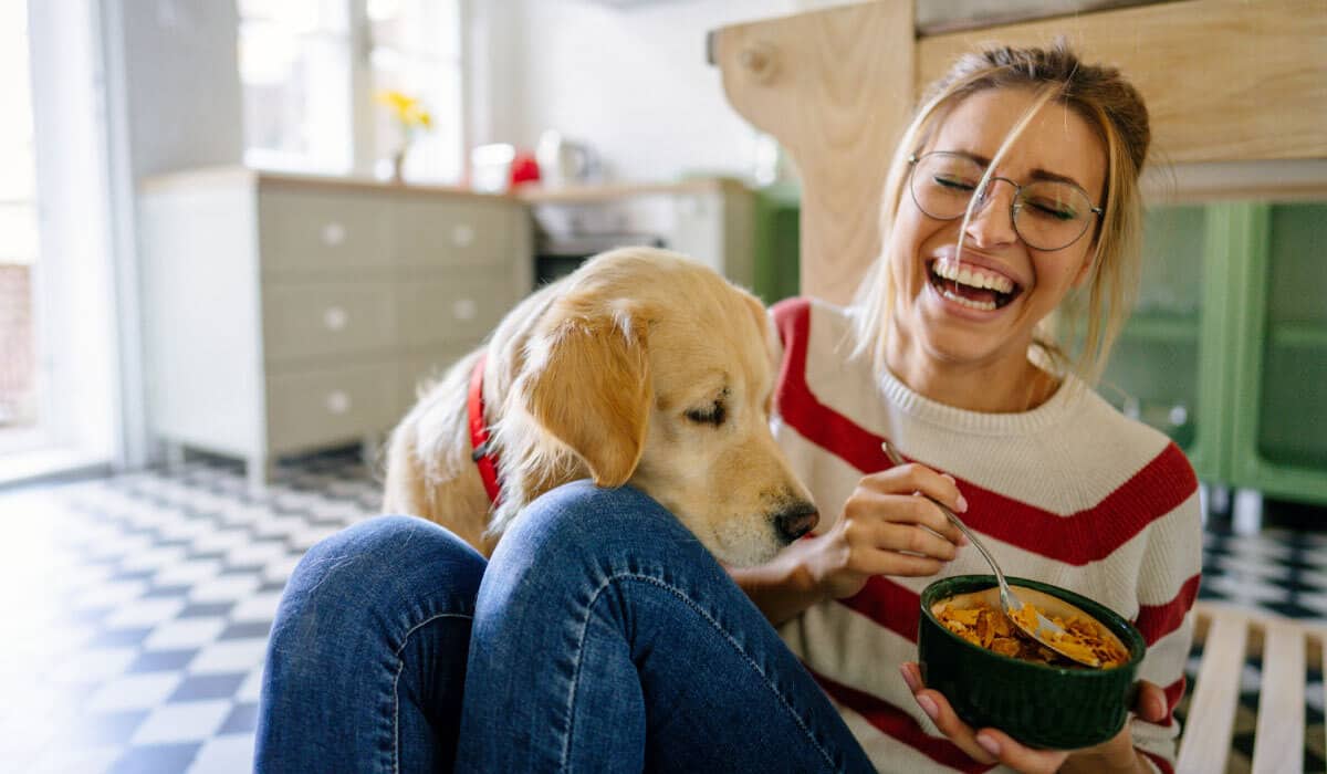 woman laughs while holding food away from dog