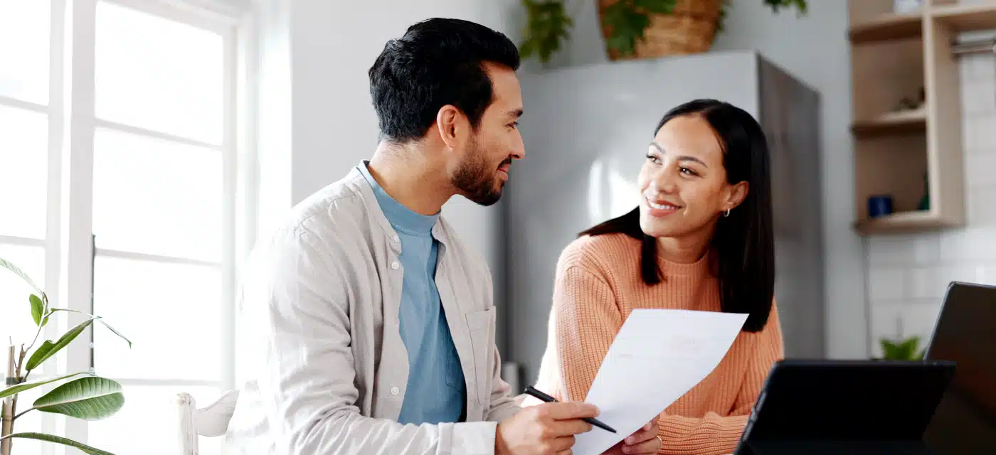Couple sitting at a kitchen table, smiling while reviewing a document together.