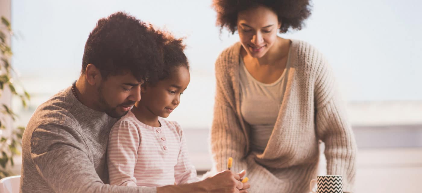 A couple looking at their young child, the child is writing on something.