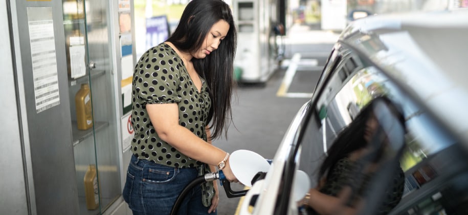 Woman fills up vehicle with gas while standing at a gas pump