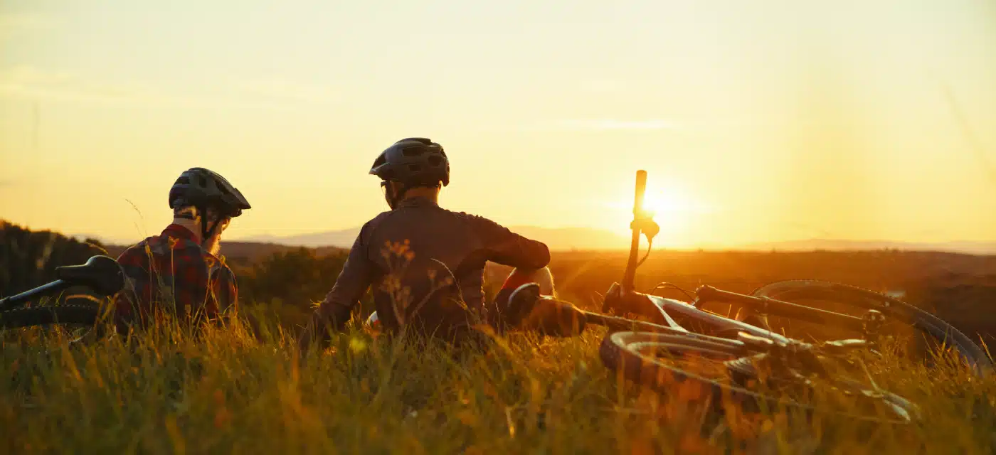 Two guys taking a break on at the top of a hill after a bike ride watching the sun set.