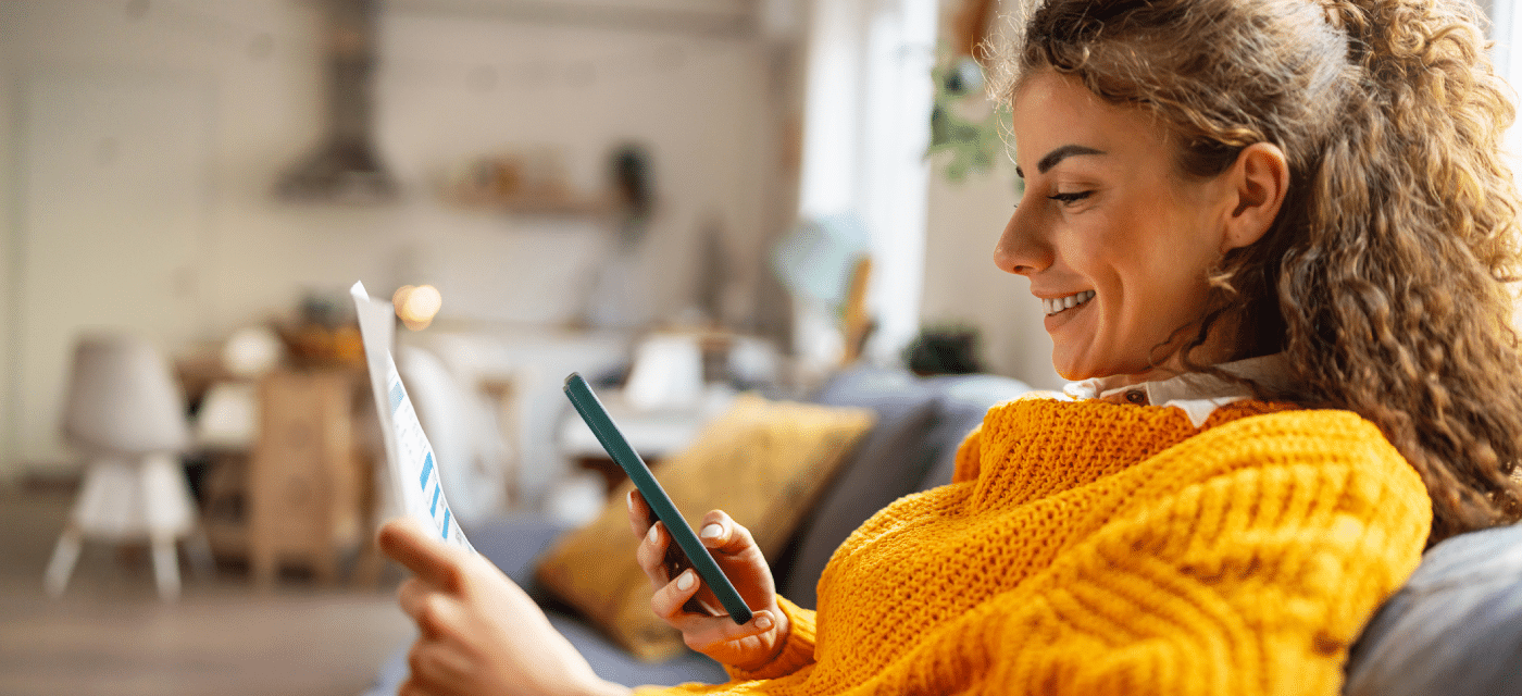 Women looking at a paper bill and comparing the information to the information on her phone.