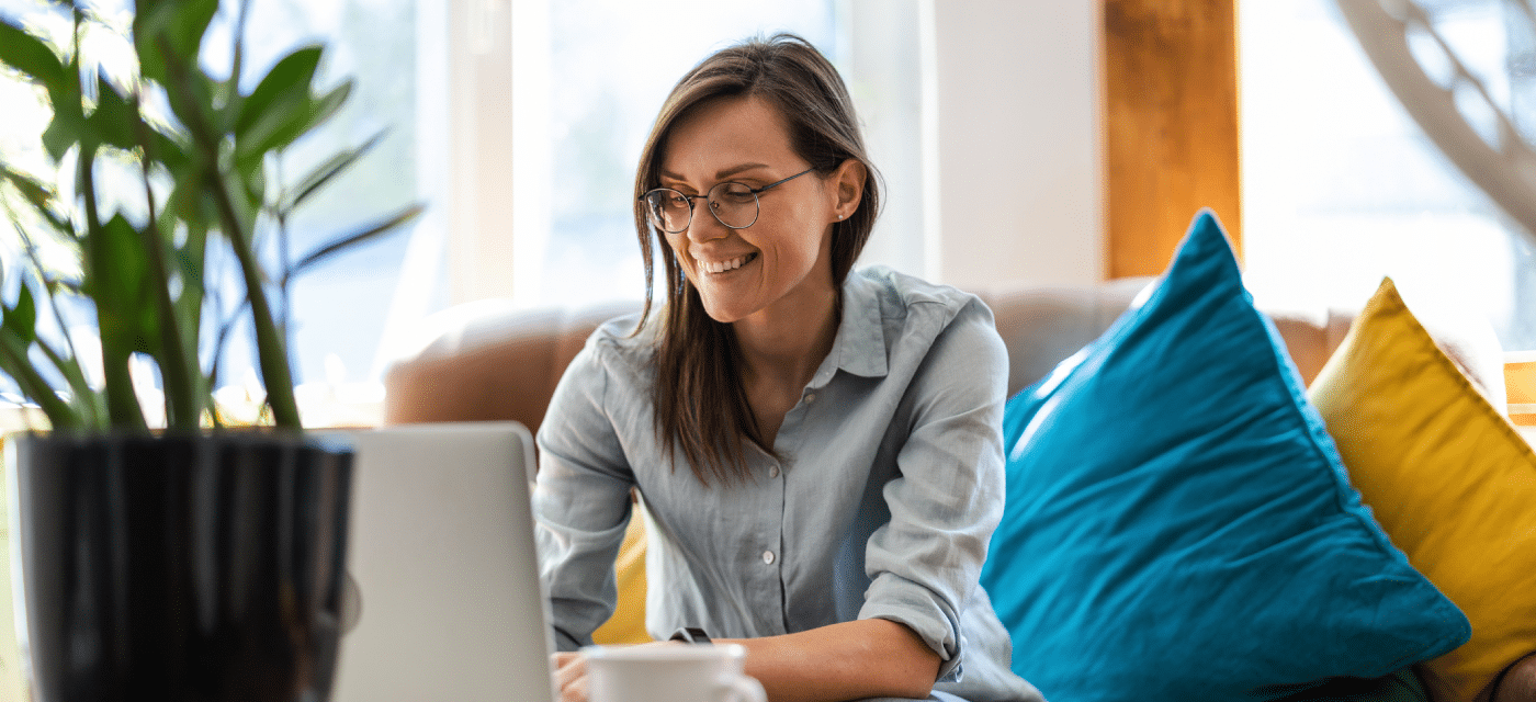 Women sitting on couch while working on her computer and smiling.