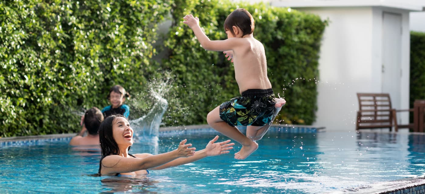 A woman and a young boy using a swimming pool. the boy is jumping into the water and the woman is catching him.
