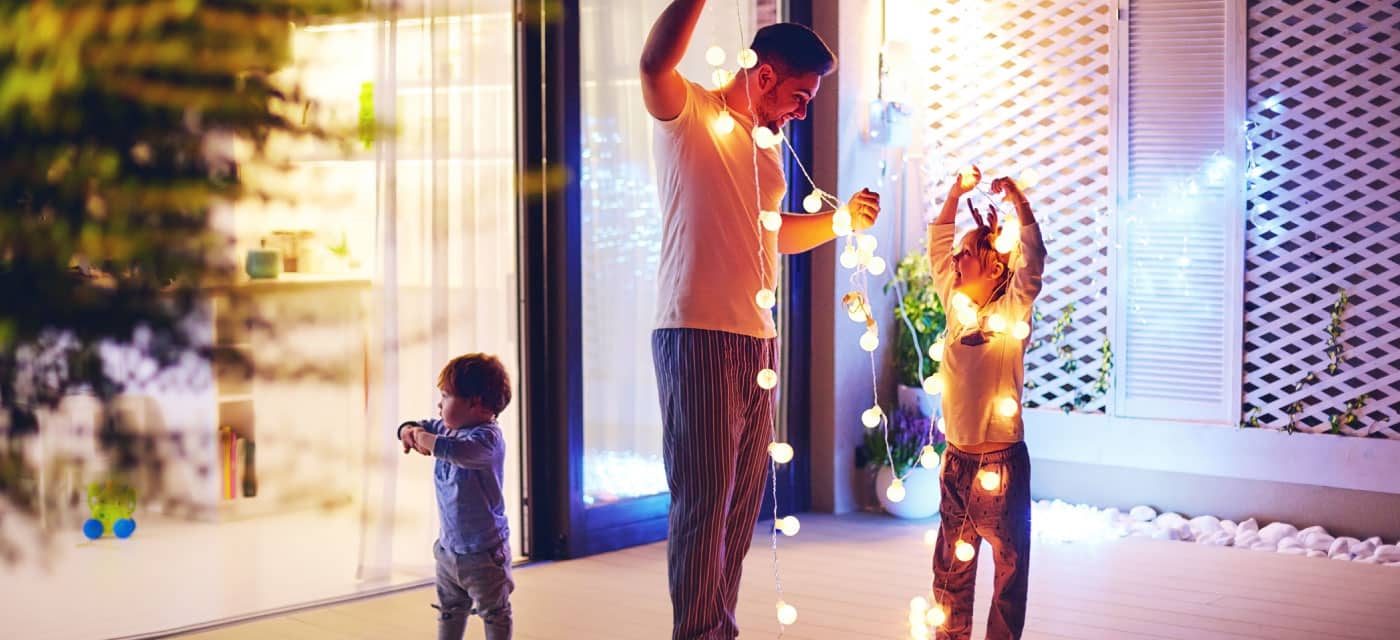 a man and two young children hanging string lights.