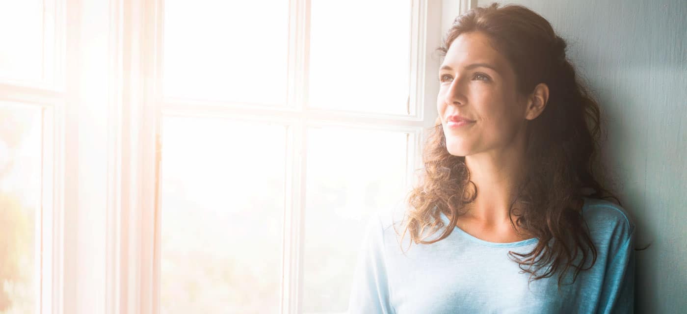 A woman staring out a window from inside a home.