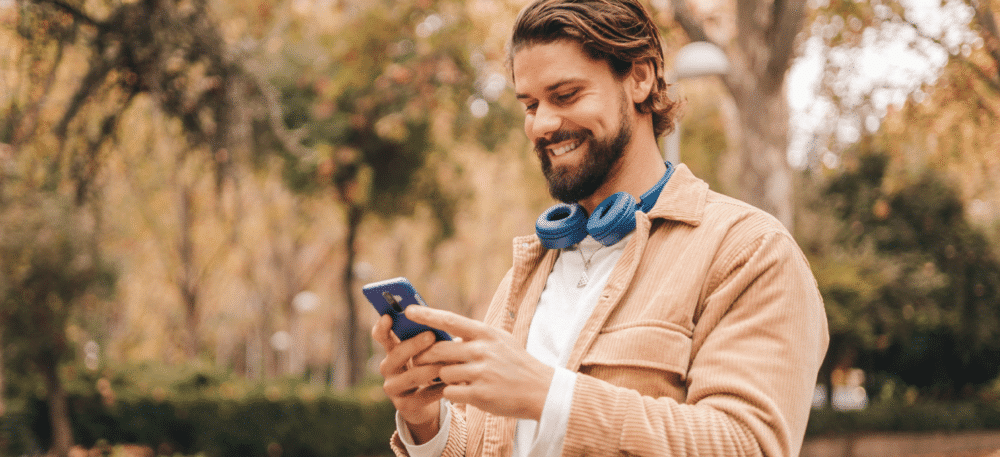 Man stands outside looking at phone with headphones around his neck.