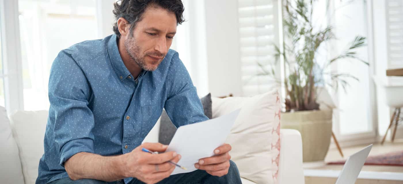 A man sitting on a couch and reading a piece of paper. of paper.
