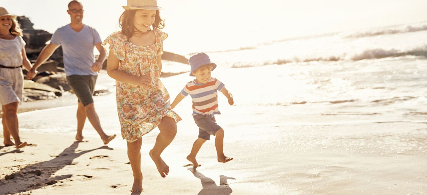 A family walking on the beach, the two children are running ahead and smiling.
