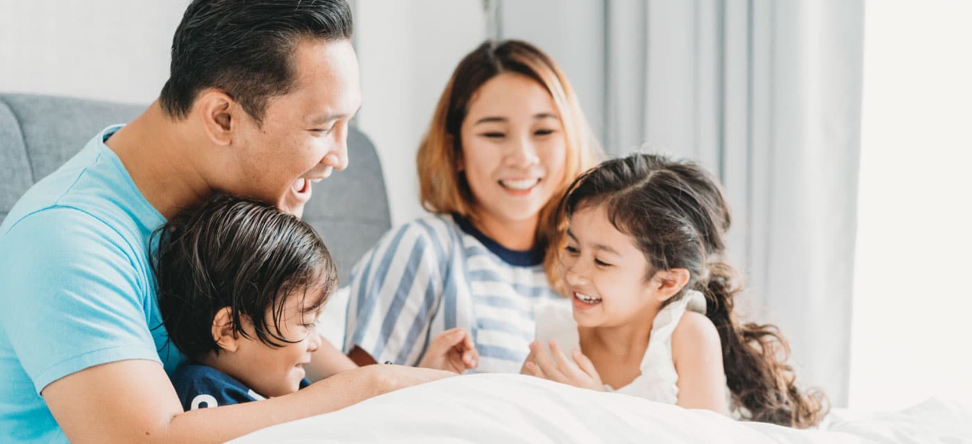 A family sitting on a couch, the kids are giggling, and the parents are smiling.