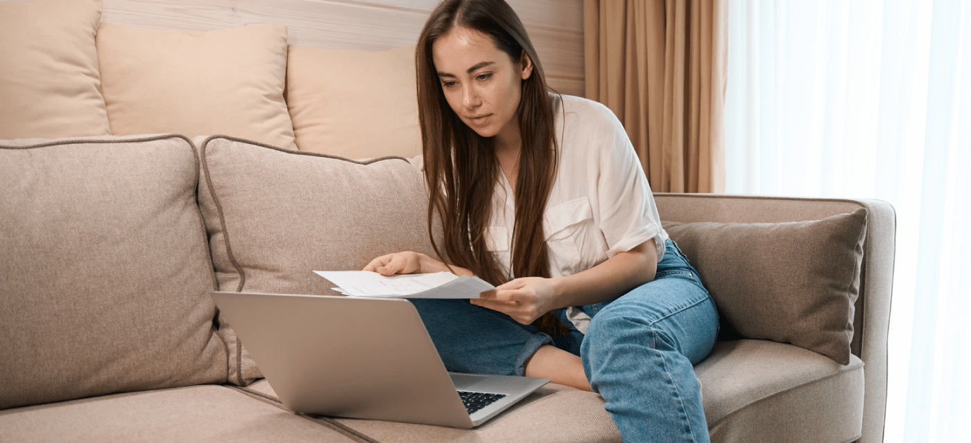 Woman looking over documents and working on a laptop.