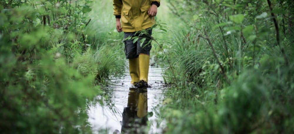 A child walking through a marshy swamp, wearing rain boots.