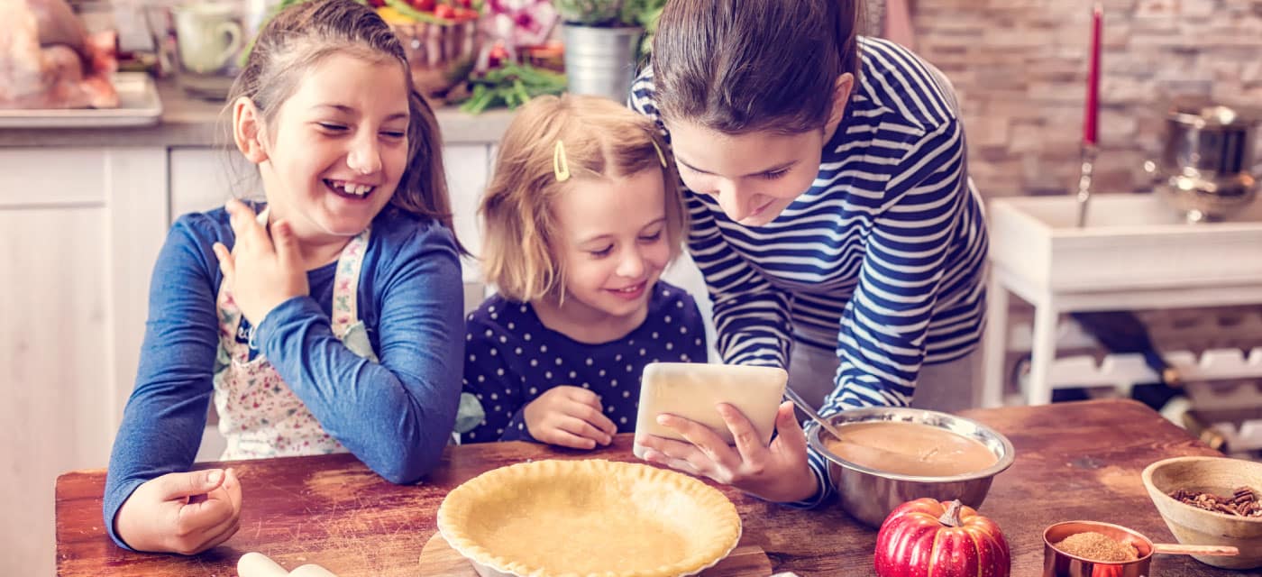 A woman and two children in a kitchen with a pie, they appear to be baking and are looking at a tablet.