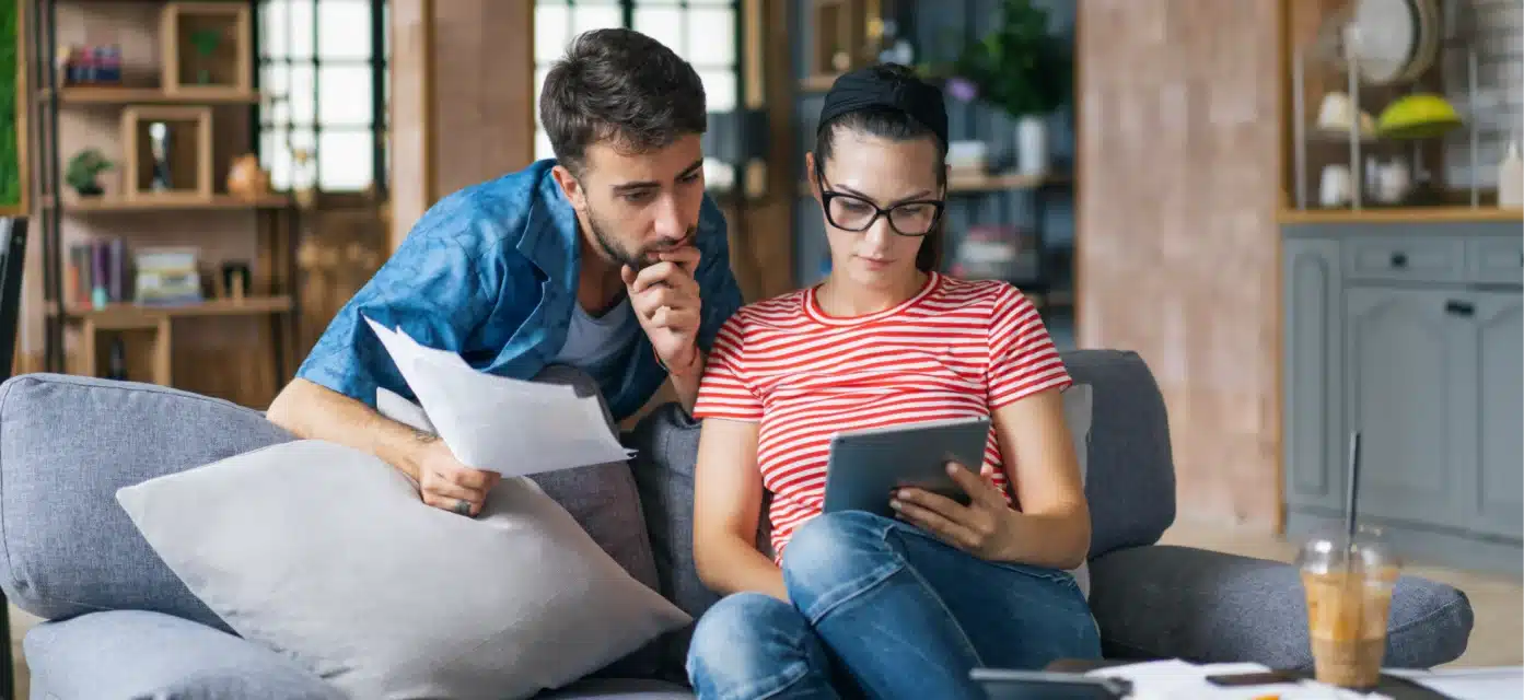 Woman and man comparing information from paper documents to information on a tablet.