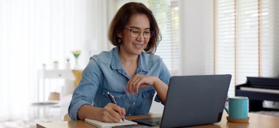 Lady in blue shirt working in front of a computer and taking notes