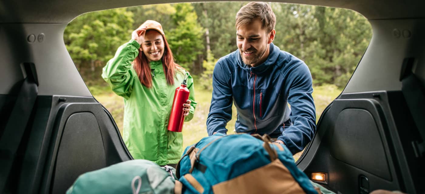 Two people preparing to go camping, they are standing in the trunk of their car looking at backpacks.