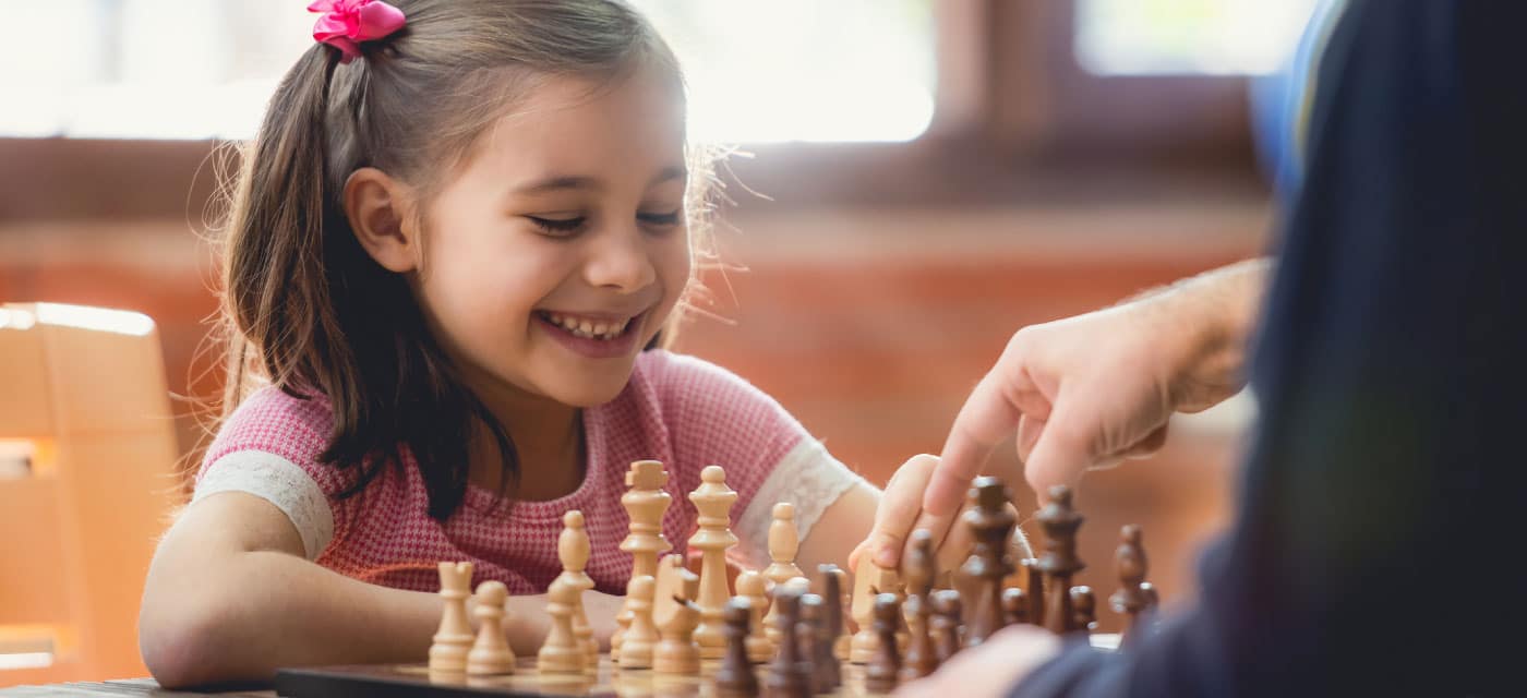 A young girl playing chess with an adult.