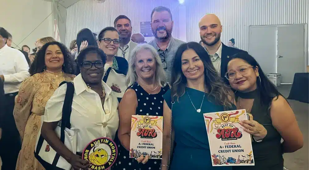 Group of smiling adults at an indoor awards event, two women in front holding certificates labeled Best of AX (awards).
