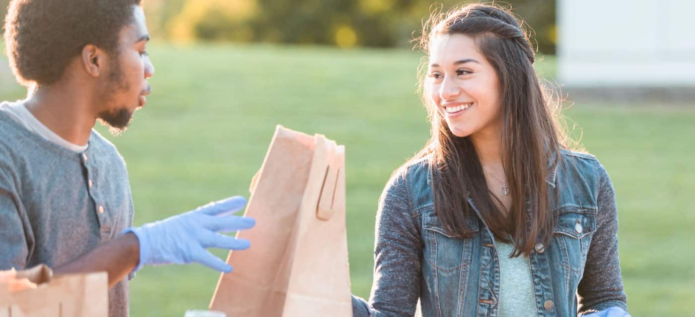 Two young people holding a paper bag. They are smiling at each other. One of them is wearing rubber gloves.