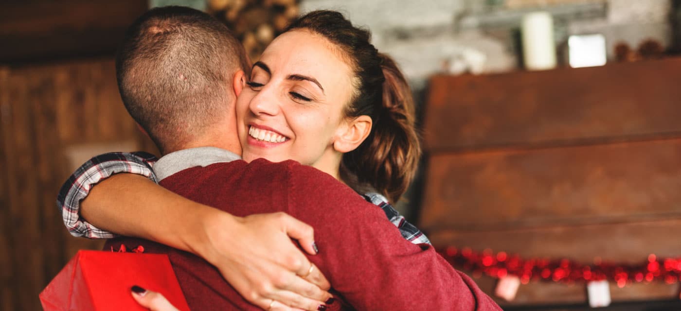 Two people hugging, one of them is holding a holiday gift.
