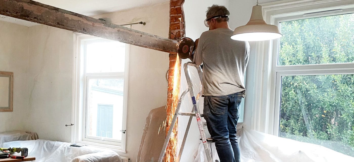 A man using a saw on a beam inside of a home.