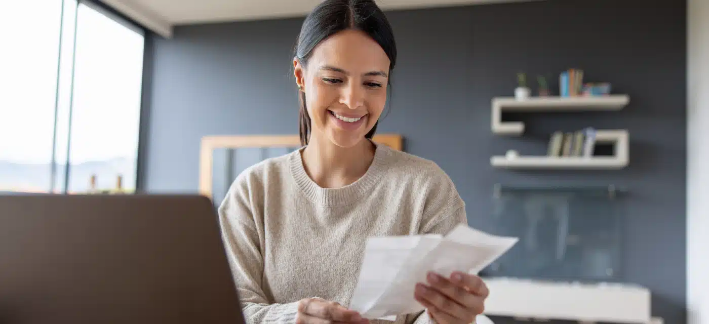 Young woman looking at receipts in front of laptop.