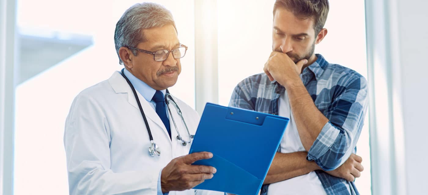 A man and a doctor looking at a clipboard. They appear concerned.