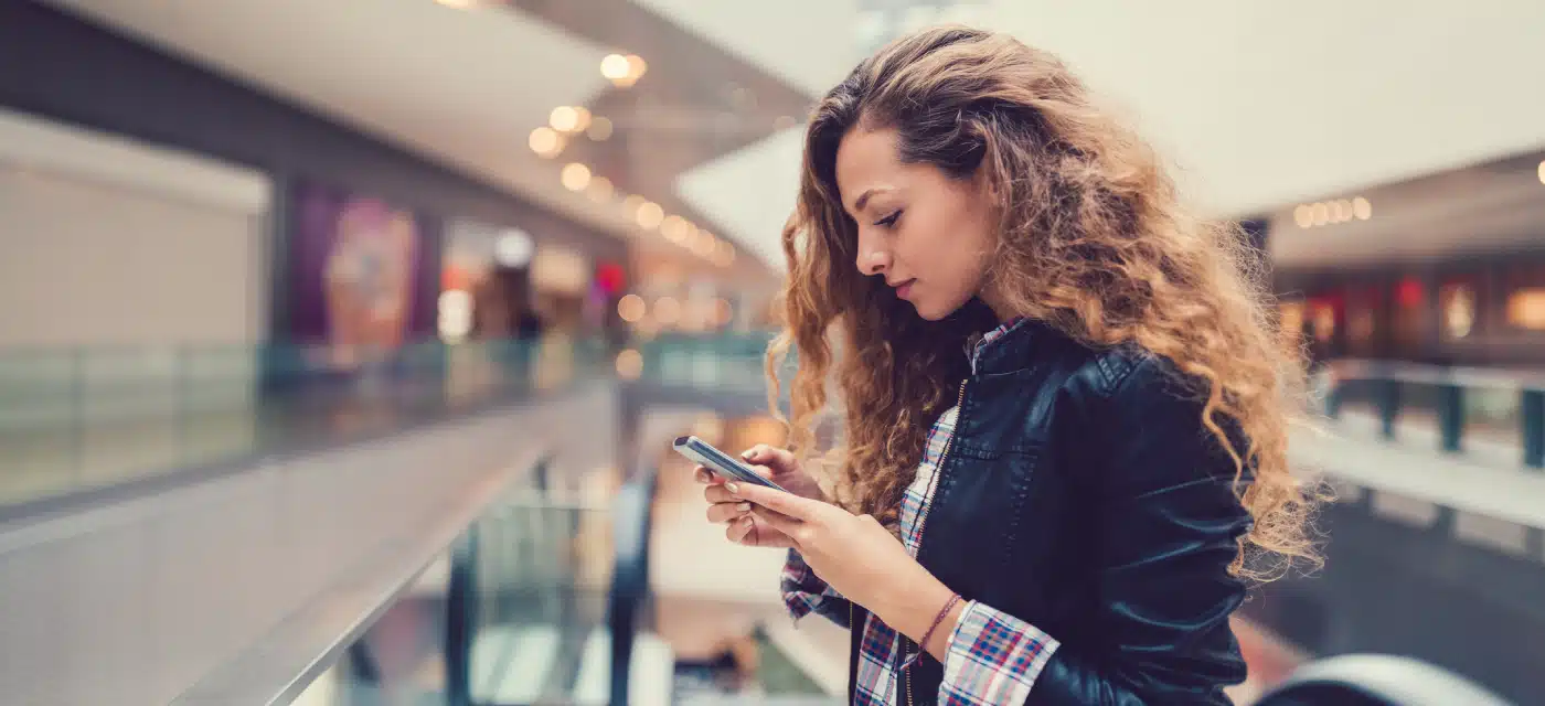 Young woman standing in the mall looking at her phone.