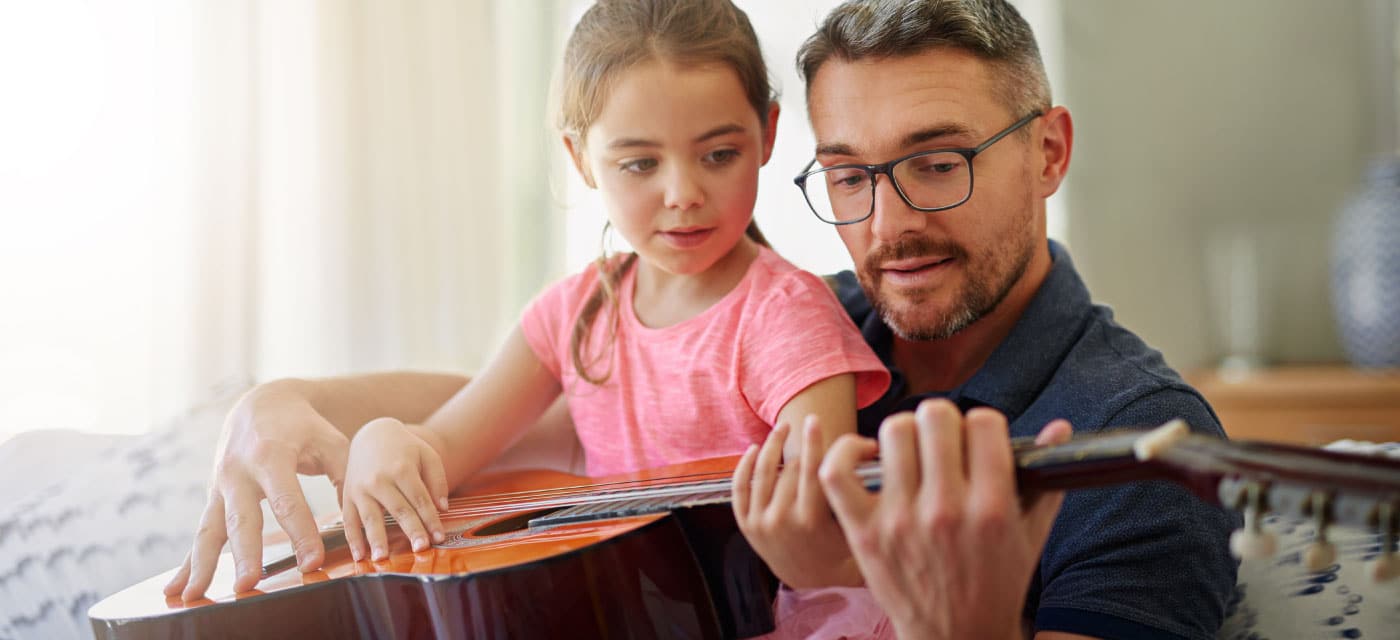 A man helping a young girl to play guitar.