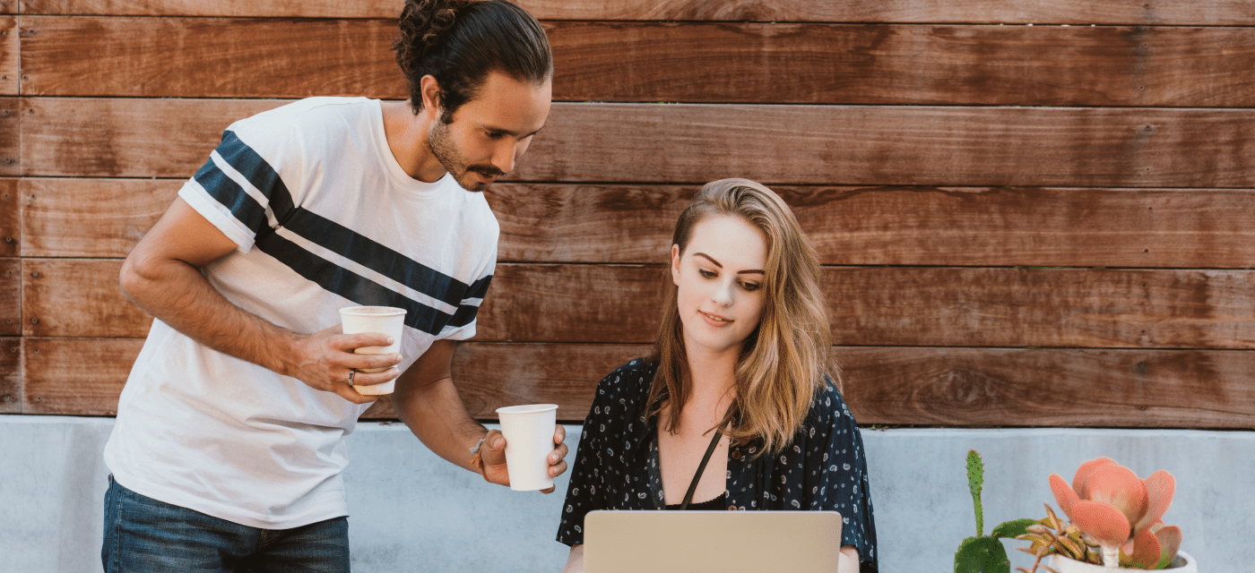 Man with drinks meeting up with a women on her computer.