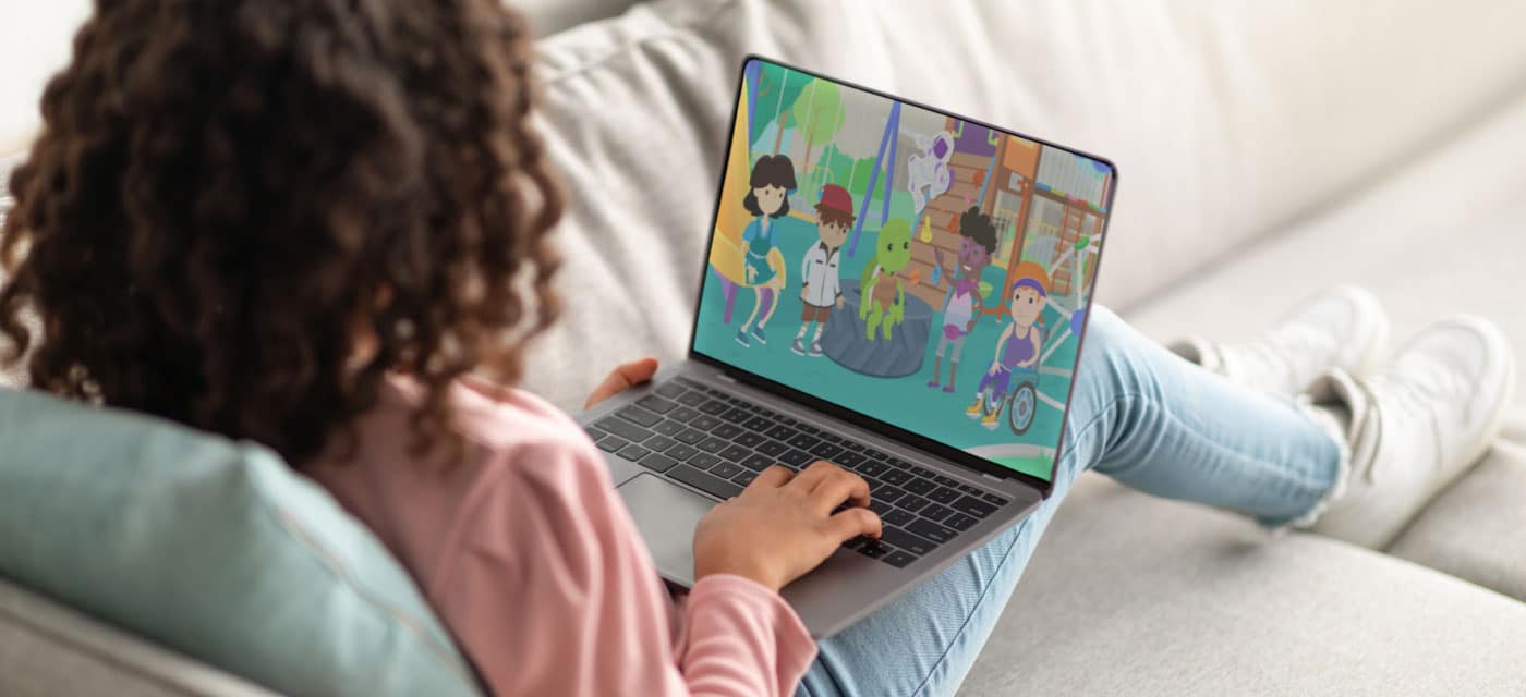 A young girl sitting on a couch, watching a cartoon on a laptop.