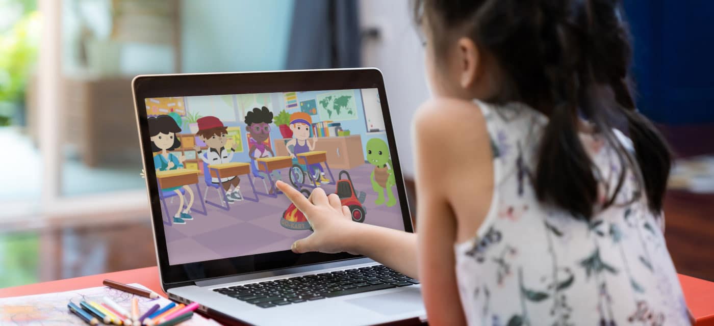 A young girl sitting at a table and watching a cartoon on a laptop.