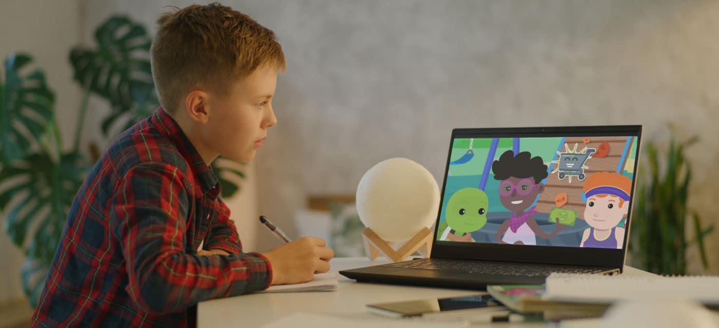 A boy sitting at a desk watching a cartoon on a laptop.