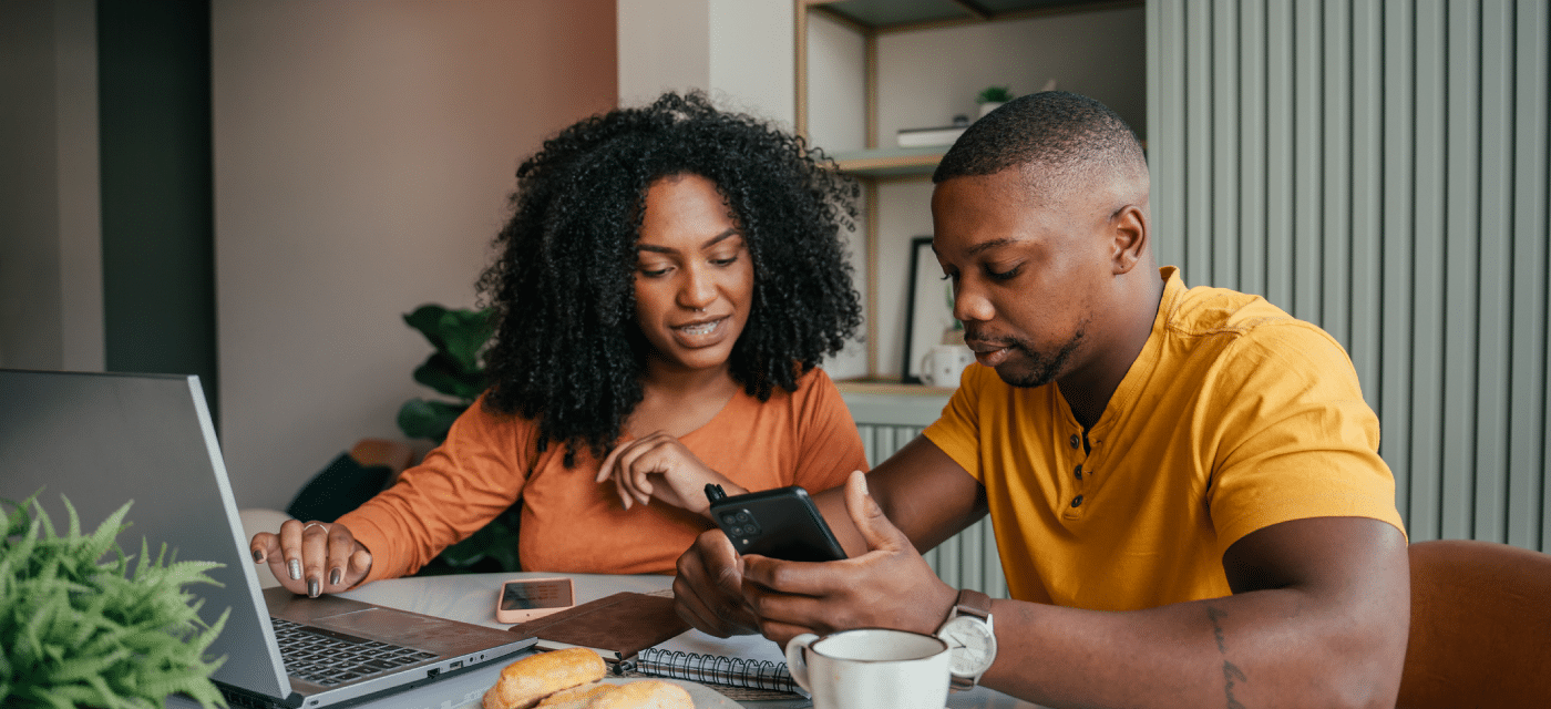 Man and women sitting at a table reviewing notes from their computer and mobile phone.