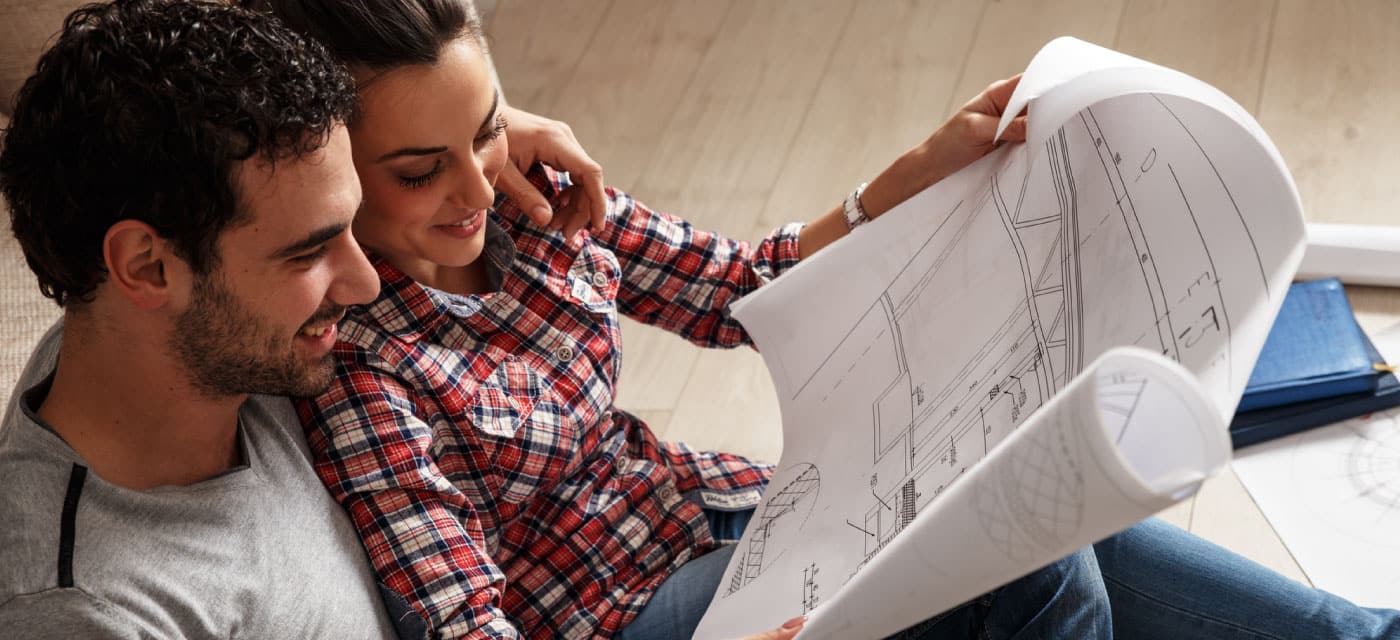couple sits on floor reviewing blueprints together