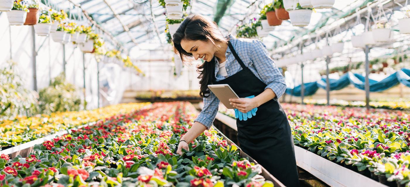 Woman in a green house checking flowers.