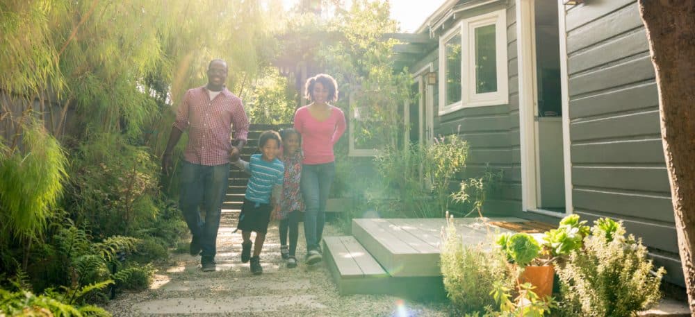 A family walking outside of a house, they are smiling.