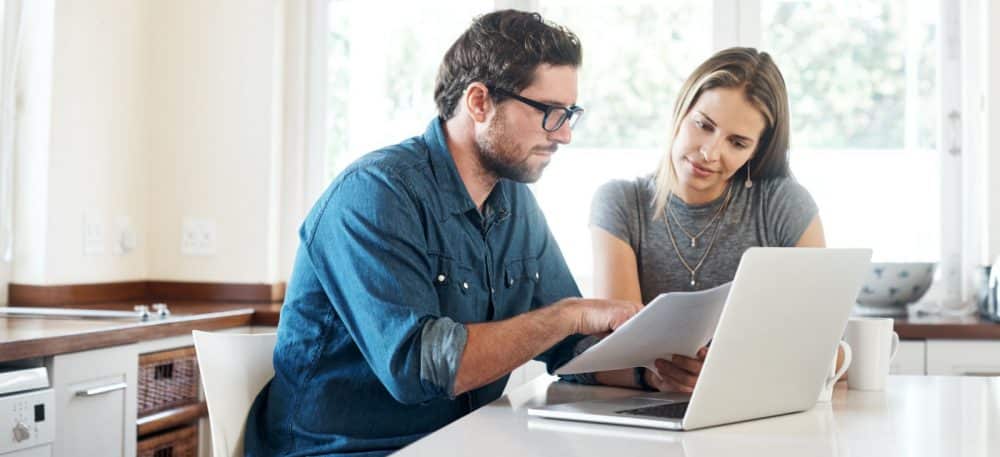 A couple standing at a table, they are looking at a laptop.