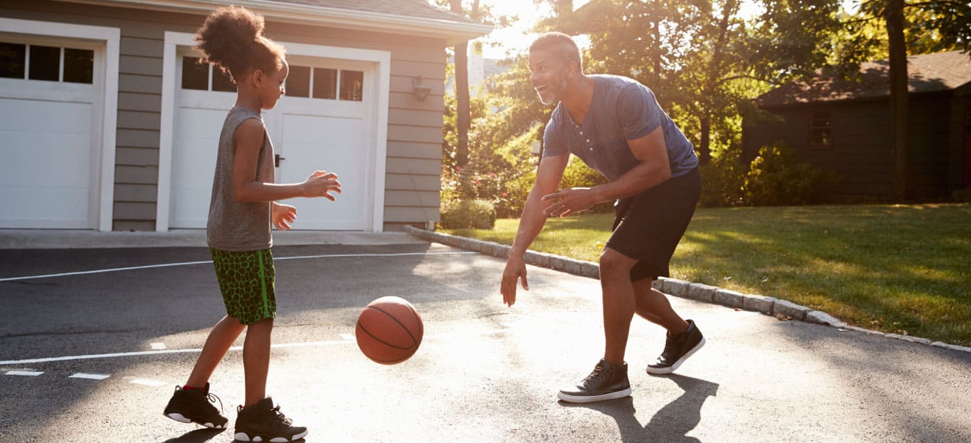 A man and a young girl playing basketball outside.