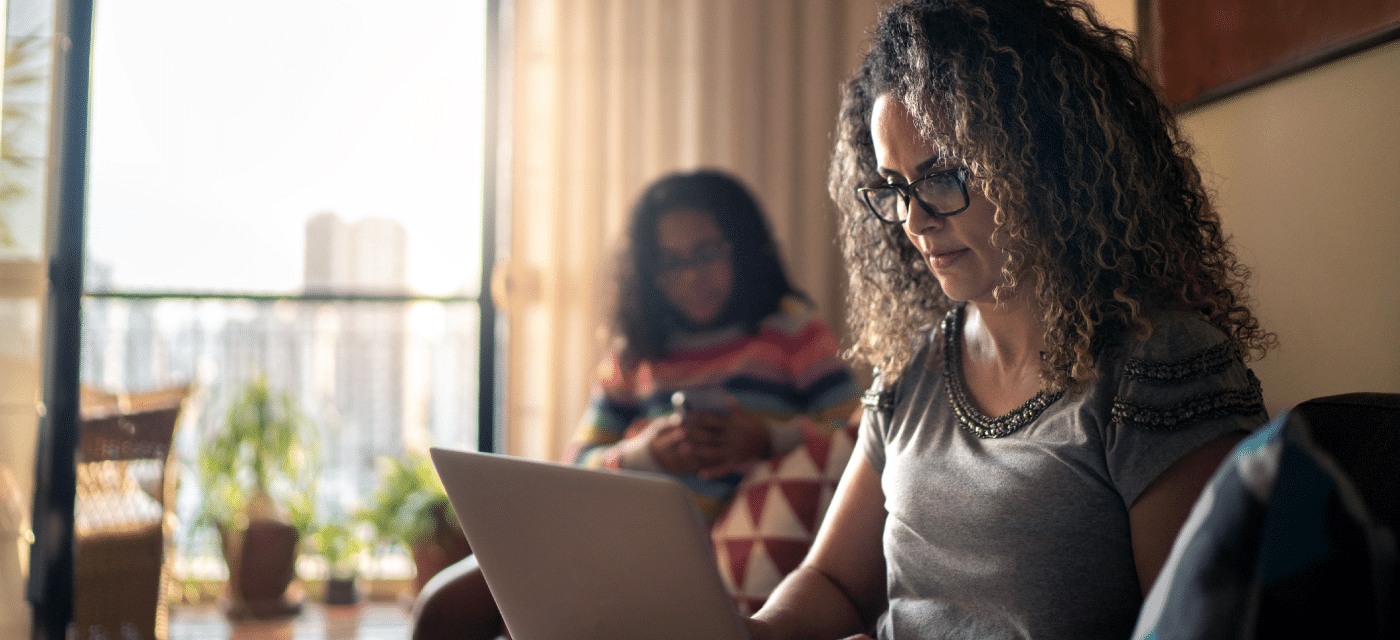 Woman working on a computer with a girl on her phone in the background.