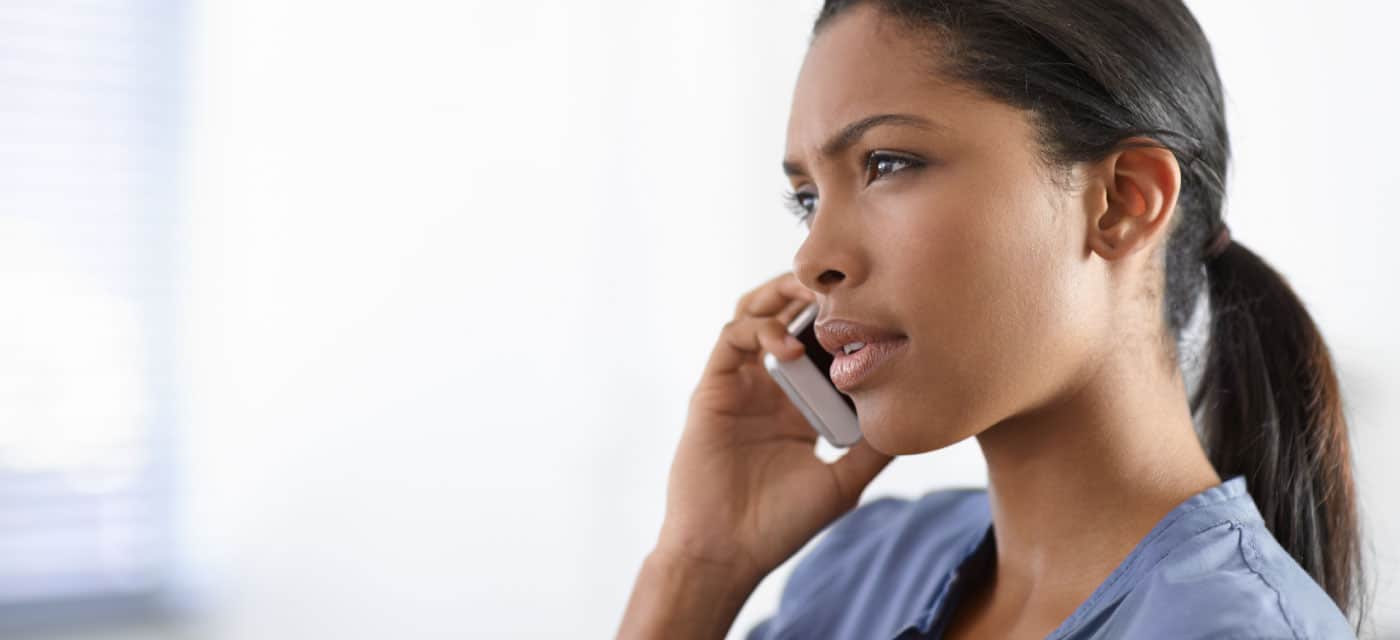 A woman is on the phone, she is holding the phone to her ear and appears worried.