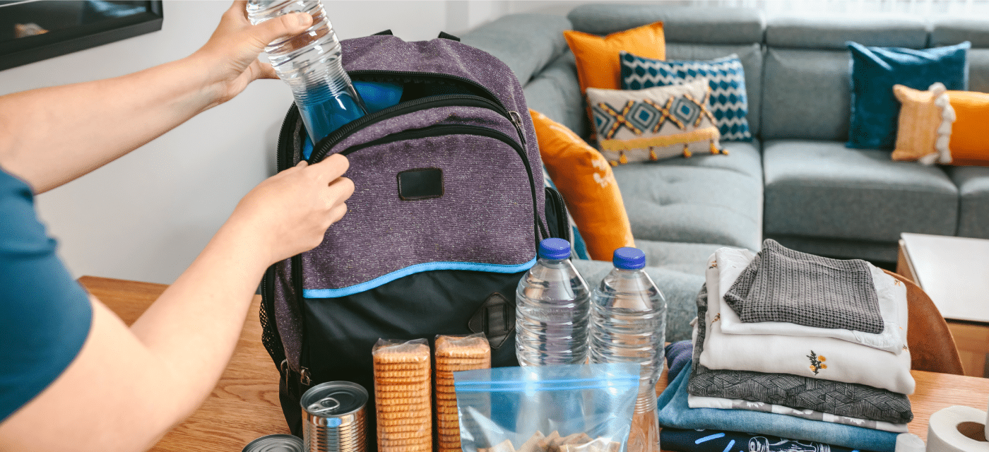 Person packs a backpack with supplies like bottled water, crackers, clothes.