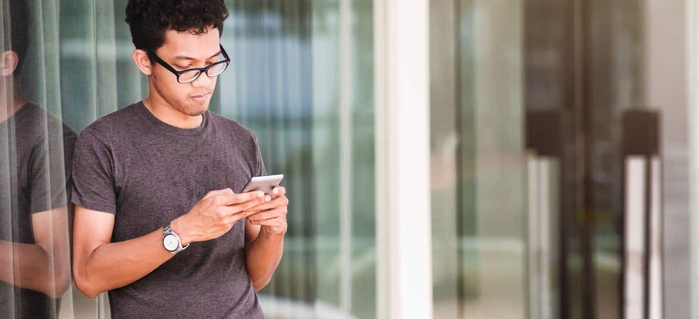 A man using a cell phone and leaning against a window.