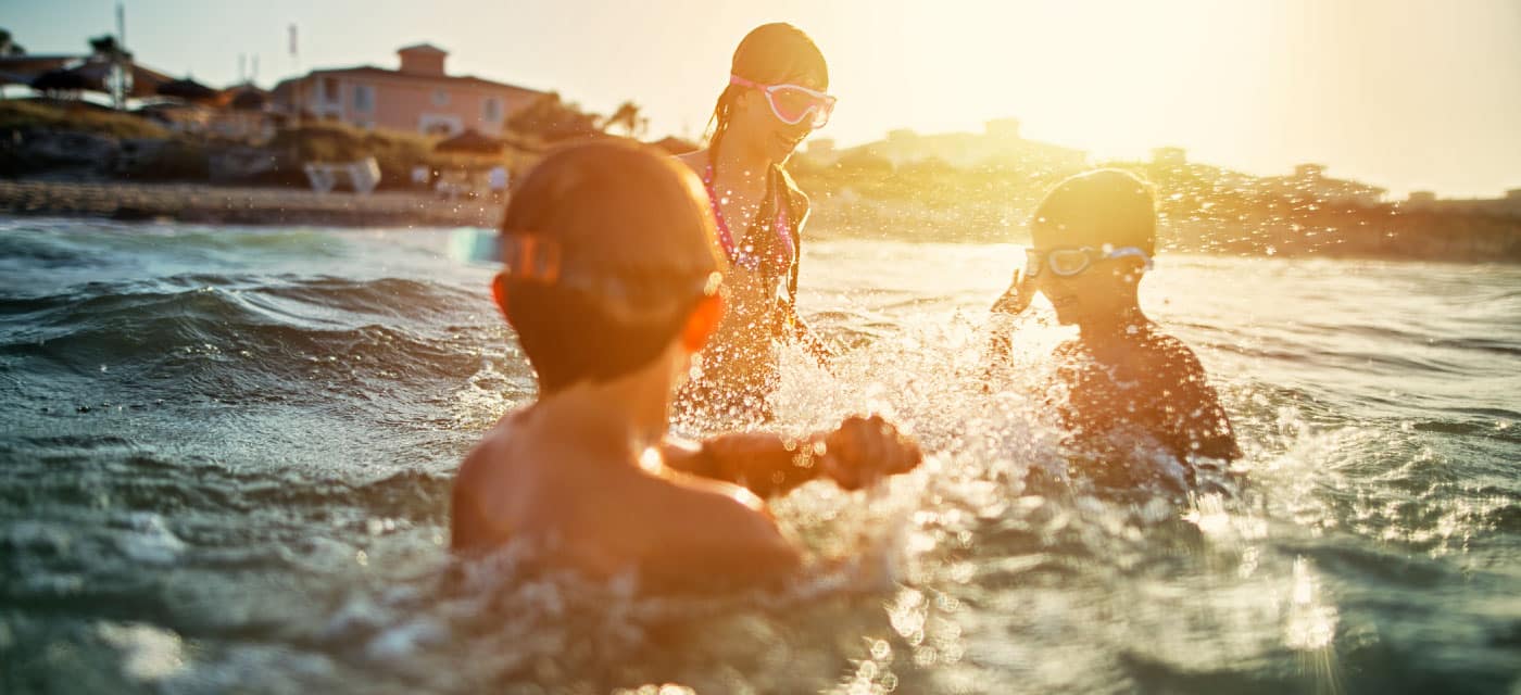 Three kids playing in the ocean, they are all wearing goggles and splashing water.