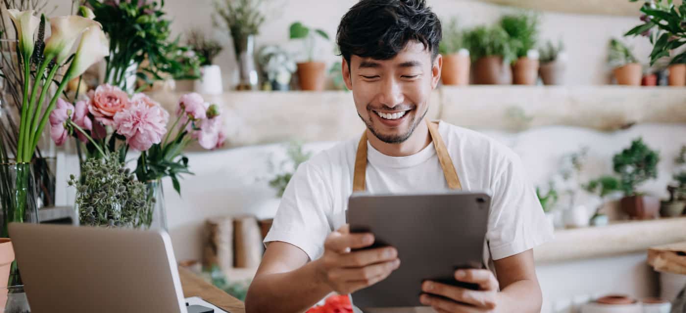 A man standing in a plant shop, he is holding an ipad and smiling.