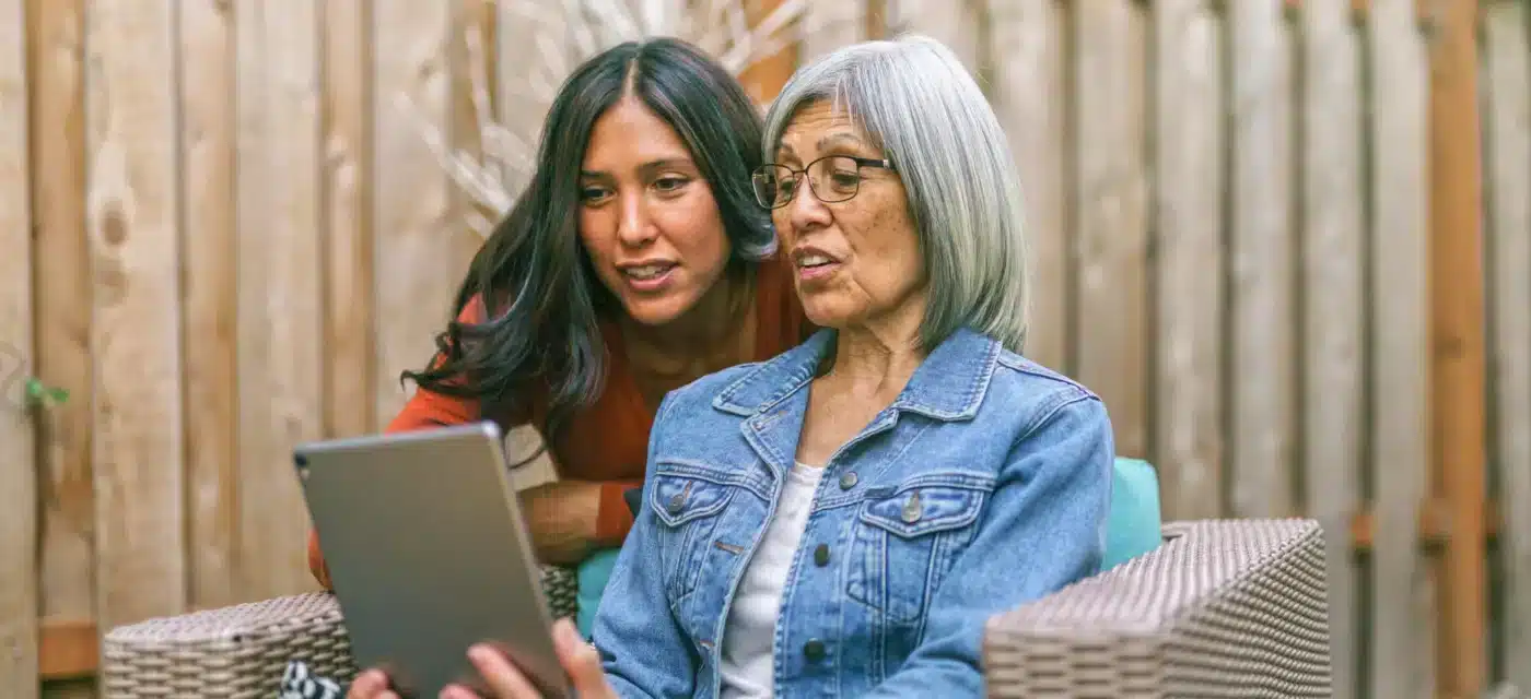 Middle aged women helps older women review information on a tablet.