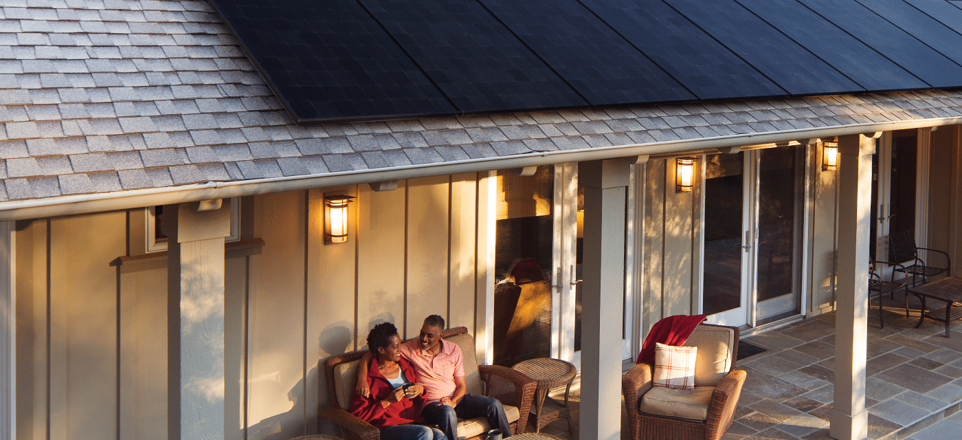 Couple sits on loveseat outside on their patio under the roof with solar panels