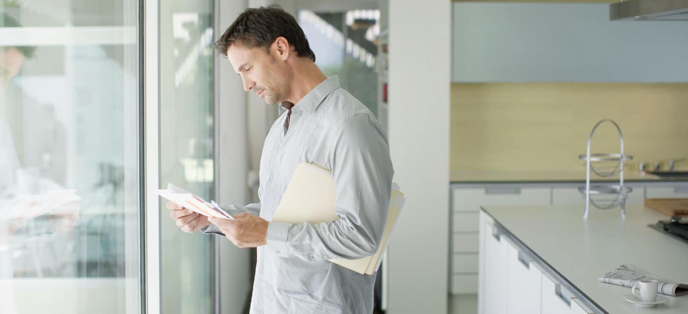 A man standing in a kitchen and looking at bills.